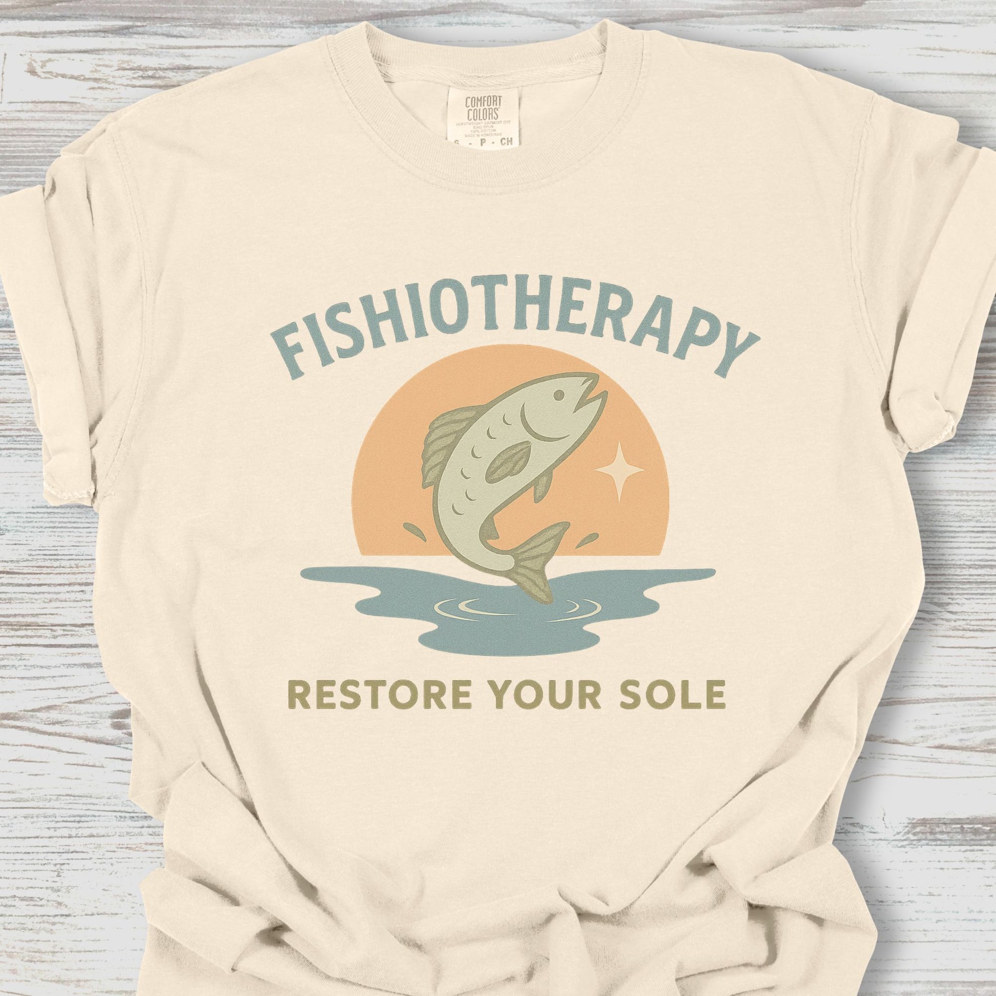 Beige t-shirt with 'Fishiotherapy' graphic and text on a wooden surface