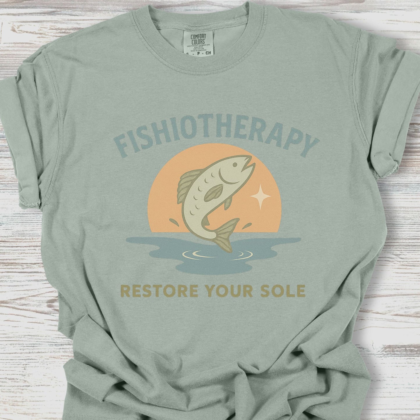 Sage green t-shirt with 'Fishiotherapy' graphic on a wooden surface