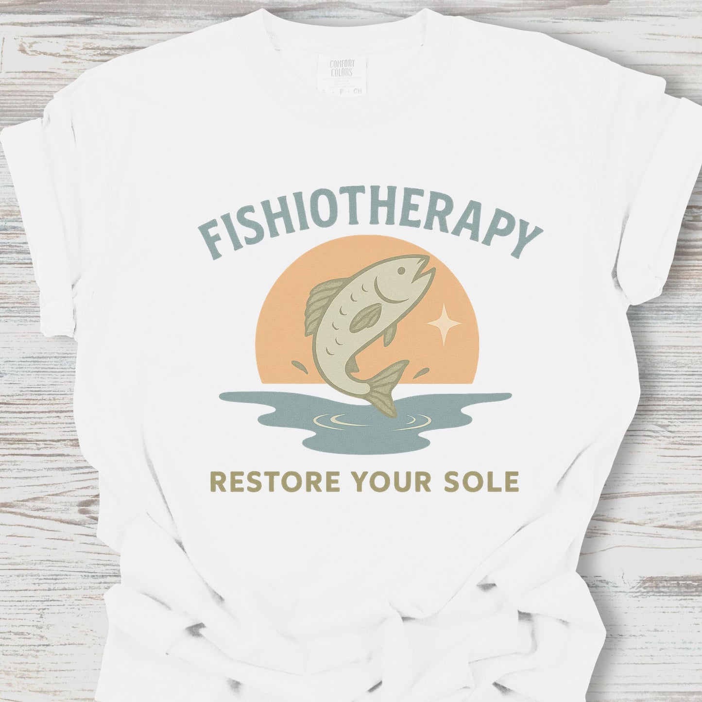 White t-shirt with 'Fishiotherapy' graphic featuring a fish and sunset on a wooden surface
