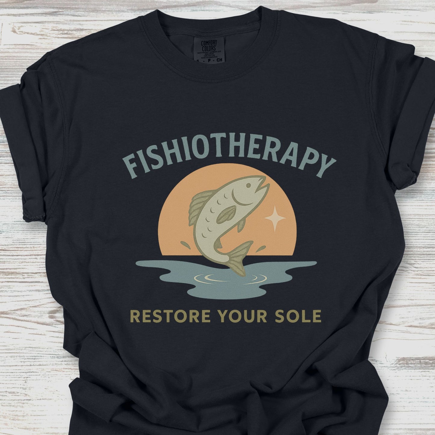 Black t-shirt with 'Fishiotherapy' graphic design featuring a fish and sunset on a wooden surface.