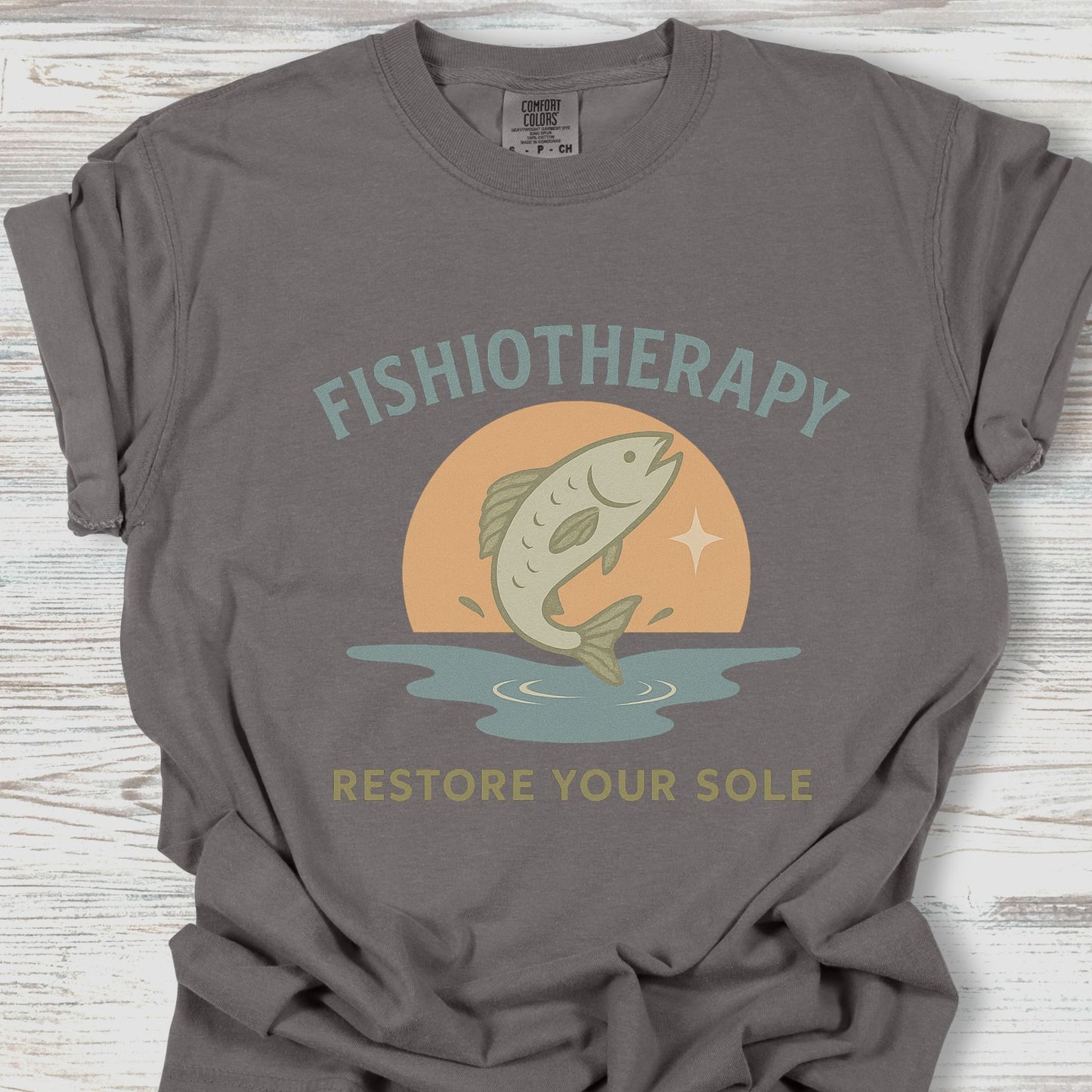 Gray t-shirt with 'Fishiotherapy' graphic design on a wooden surface
