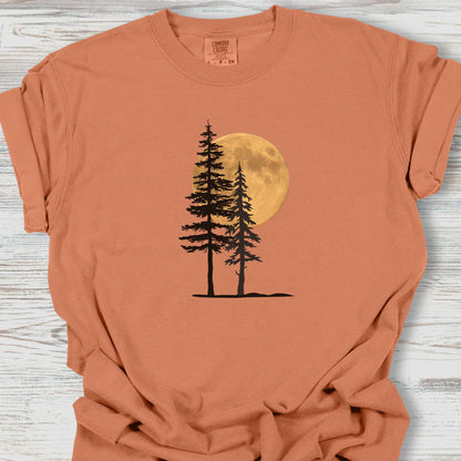 Orange t-shirt with a graphic of two trees and a moon on a wooden surface