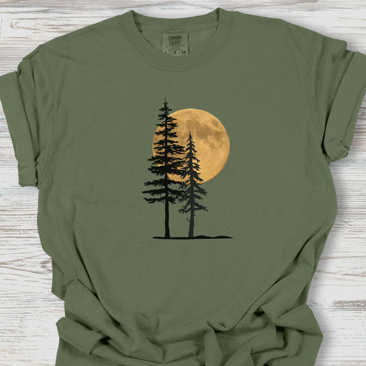 Green t-shirt with a graphic of two trees and a moon on a wooden surface