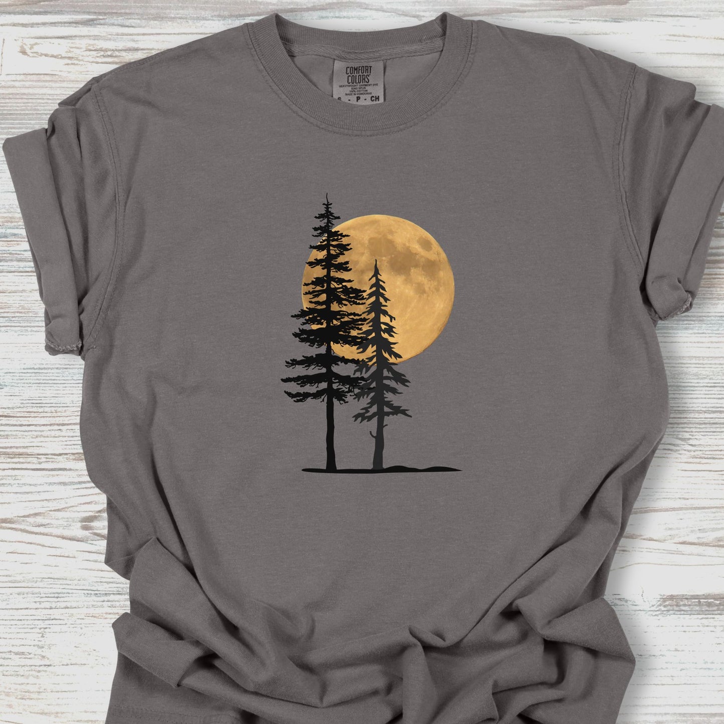 Gray t-shirt with a graphic of two trees and a full moon on a wooden surface