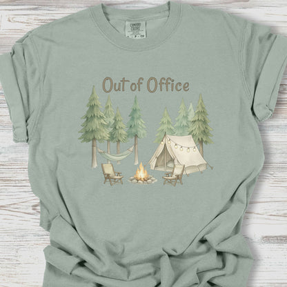 Sage green t-shirt with camping graphic and 'Out of Office' text on a wooden surface