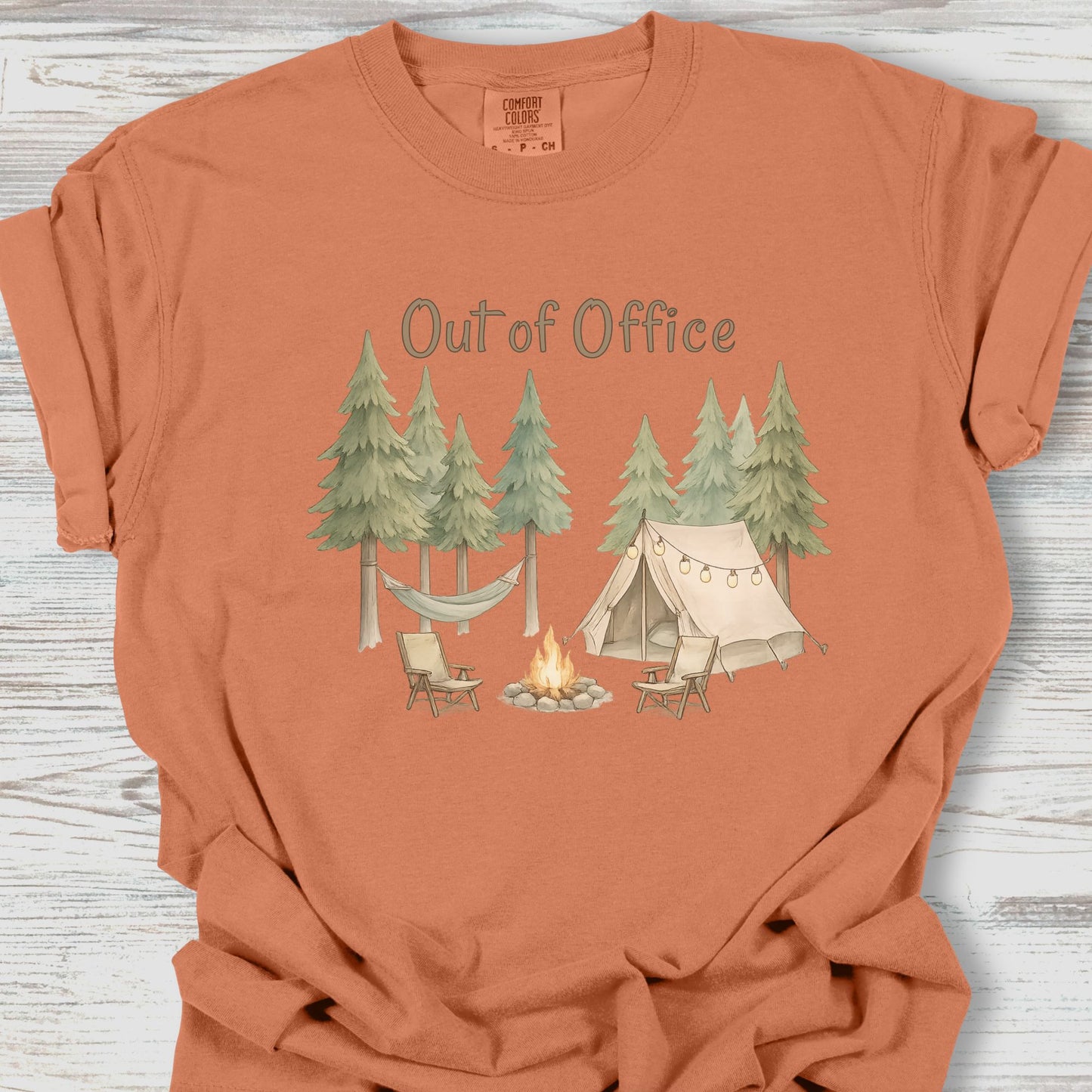 Coral t-shirt with camping graphic and 'Out of Office' text on a wooden surface