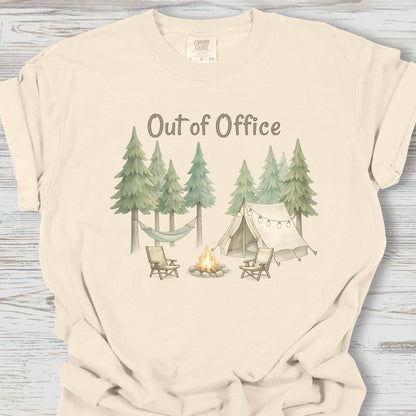 Beige t-shirt with a camping graphic and 'Out of Office' text on a wooden surface