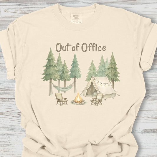 Beige t-shirt with a camping graphic and 'Out of Office' text on a wooden surface
