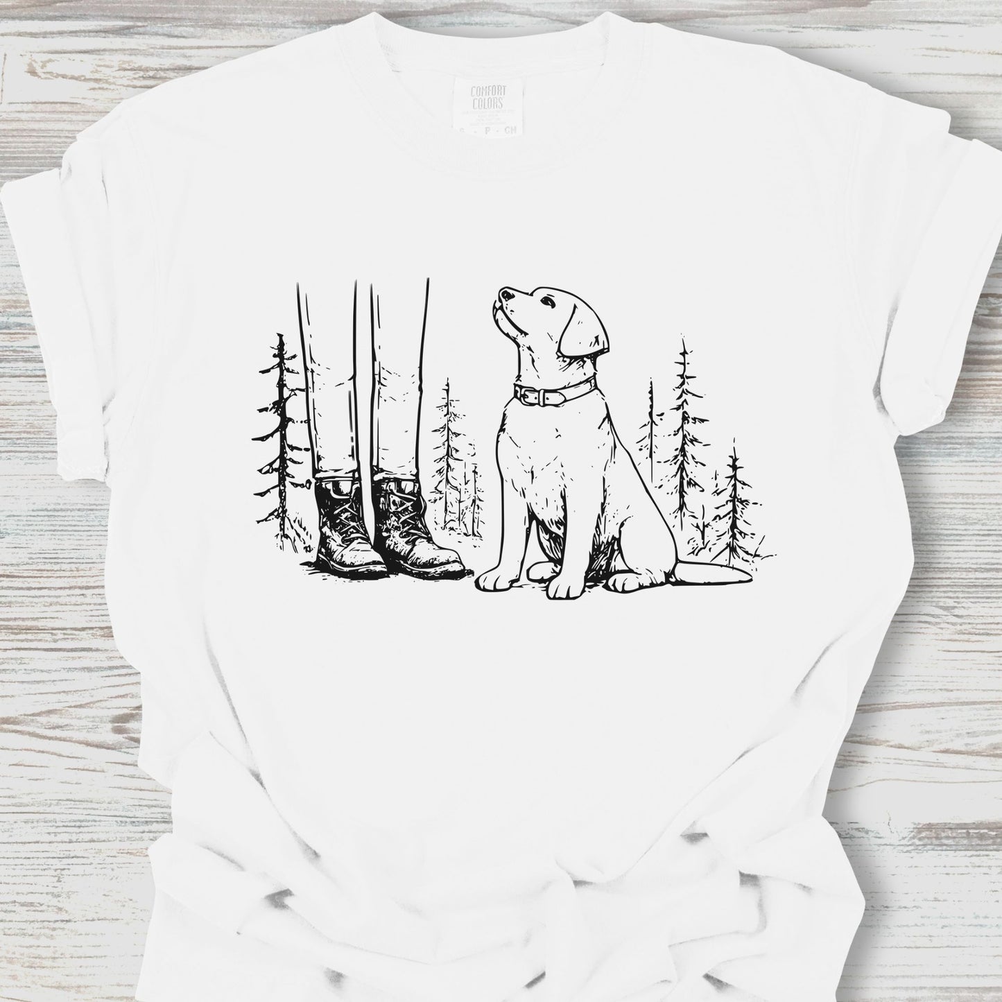 White t-shirt with a black line drawing of a dog sitting in a forest on a wooden surface.