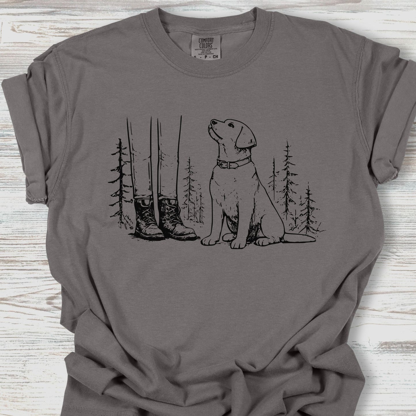 Gray t-shirt with a graphic of a dog and boots in a forest on a wooden surface