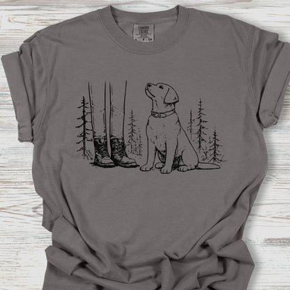Gray t-shirt with a graphic of a dog and boots in a forest on a wooden surface
