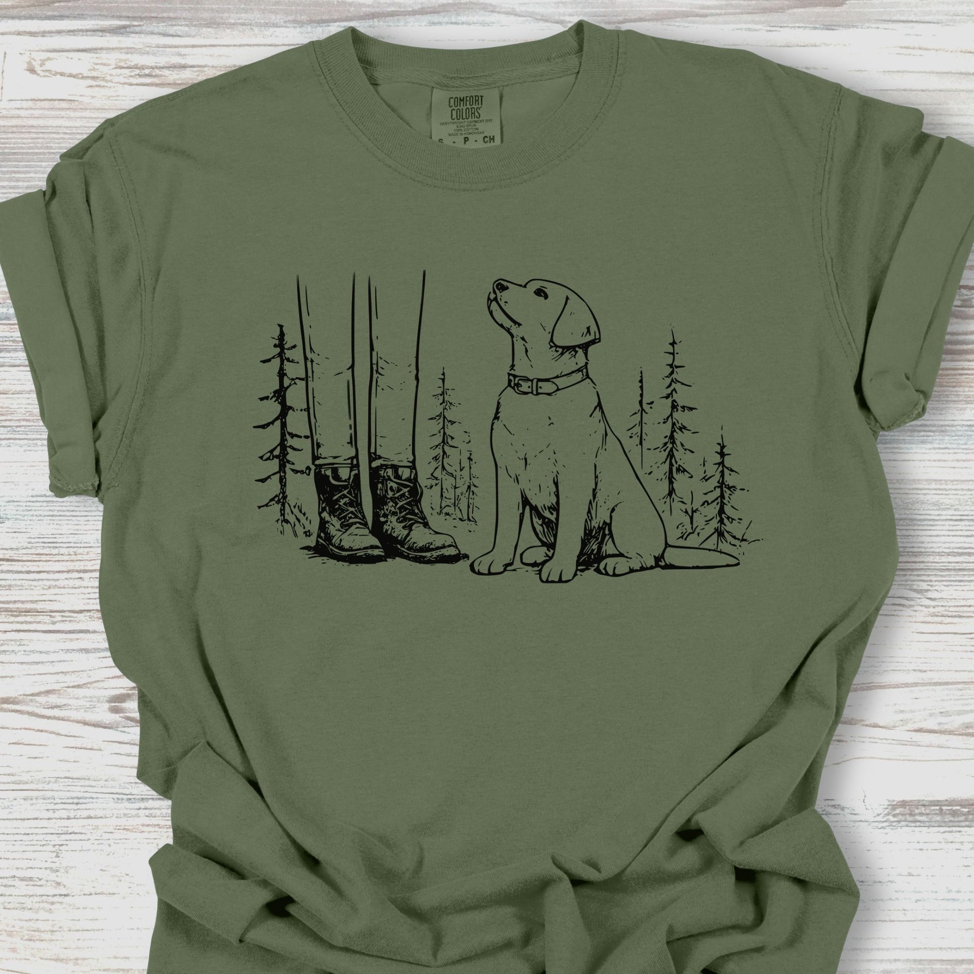 Green t-shirt with a graphic of a dog, boots, and trees on a wooden surface