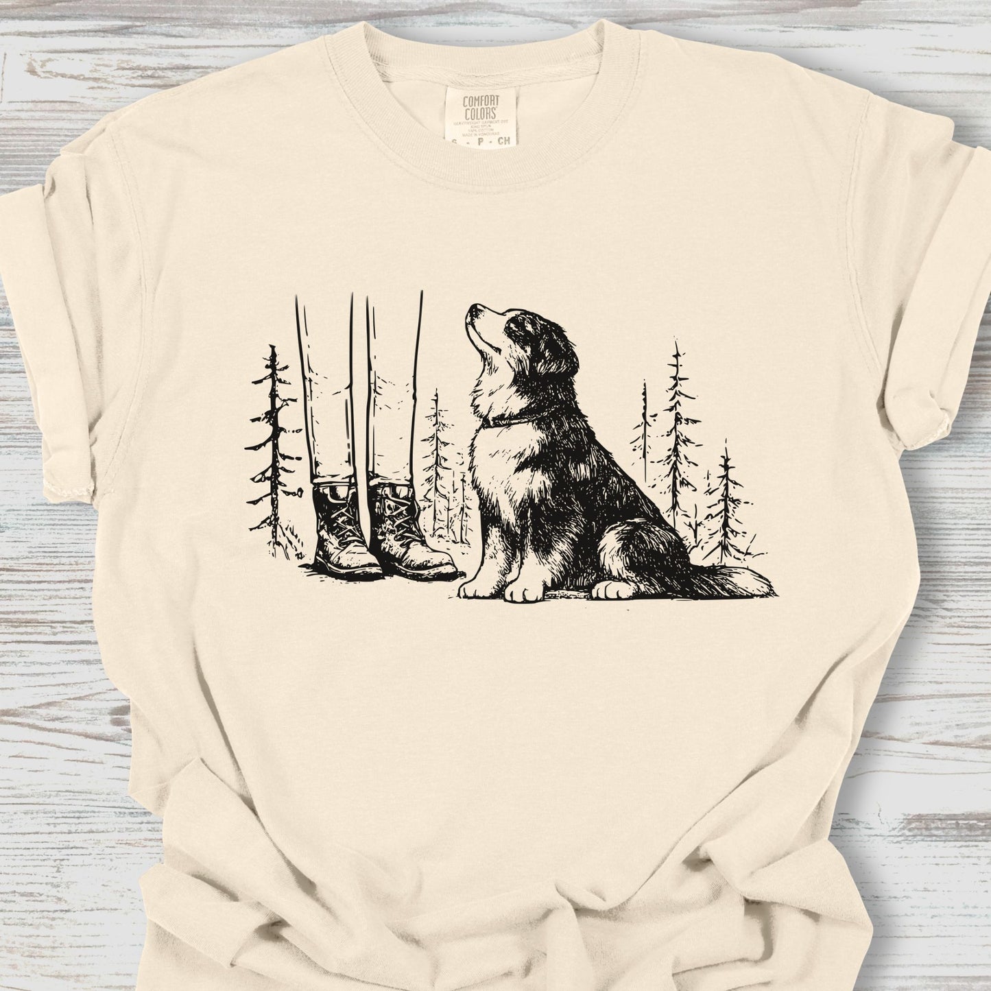 Beige t-shirt with a graphic of a dog and boots in a forest on a wooden surface