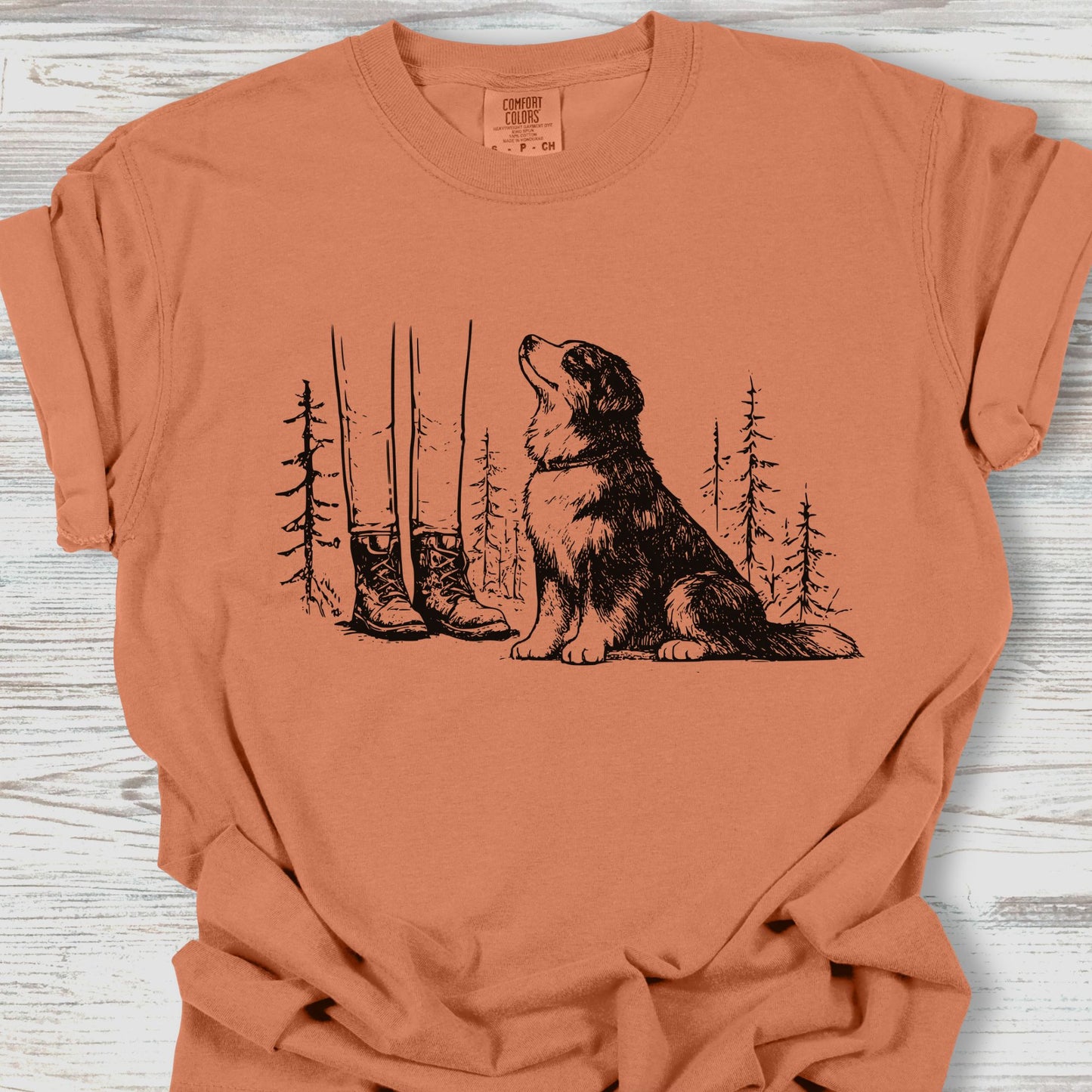 Orange t-shirt with a dog and nature graphic on a wooden surface