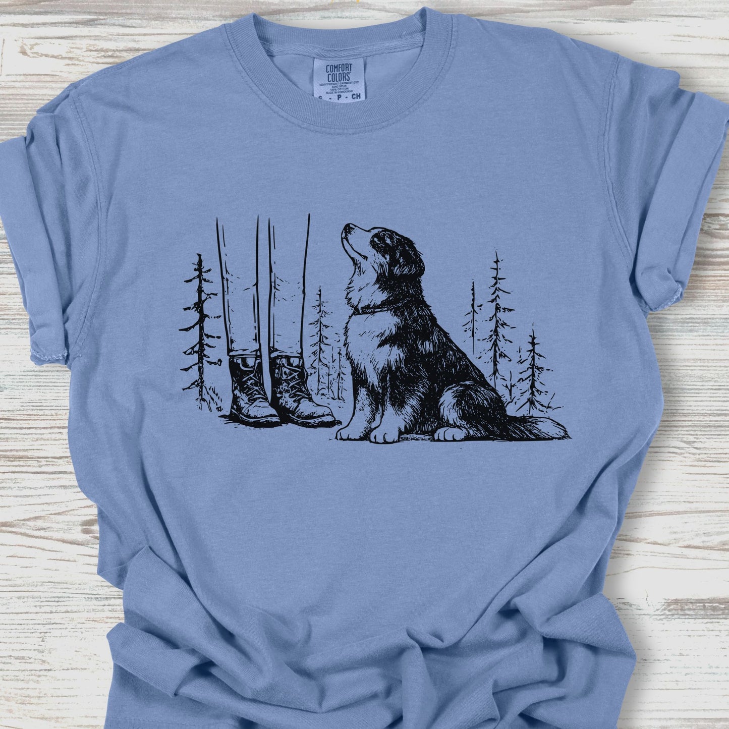Blue t-shirt with a dog and nature graphic on a wooden surface