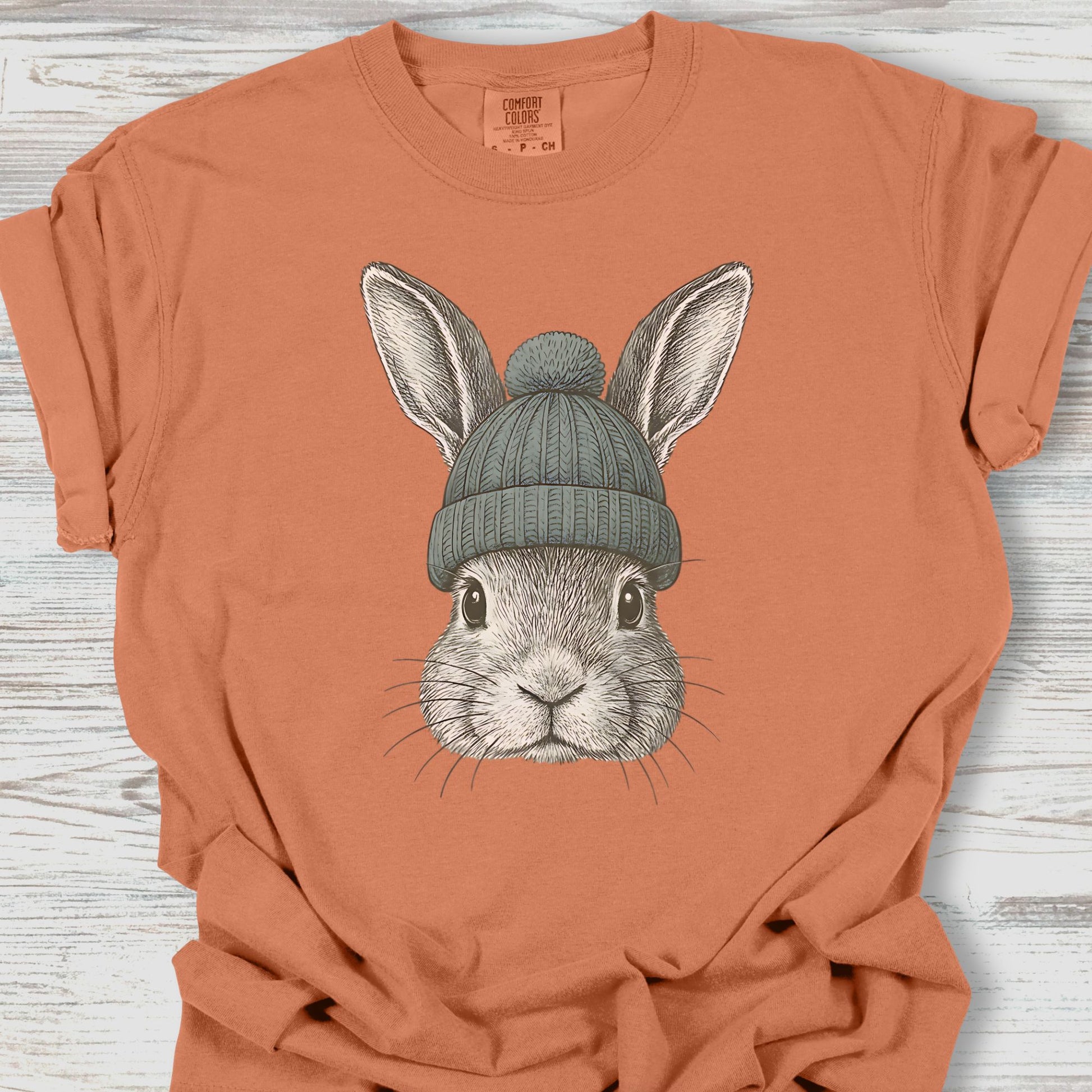Orange t-shirt with a rabbit wearing a green beanie on a wooden surface