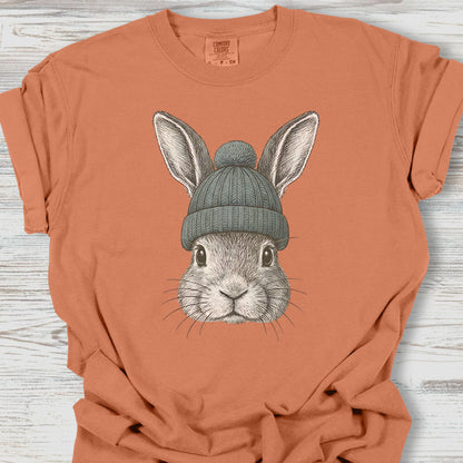 Orange t-shirt with a rabbit wearing a green beanie on a wooden surface