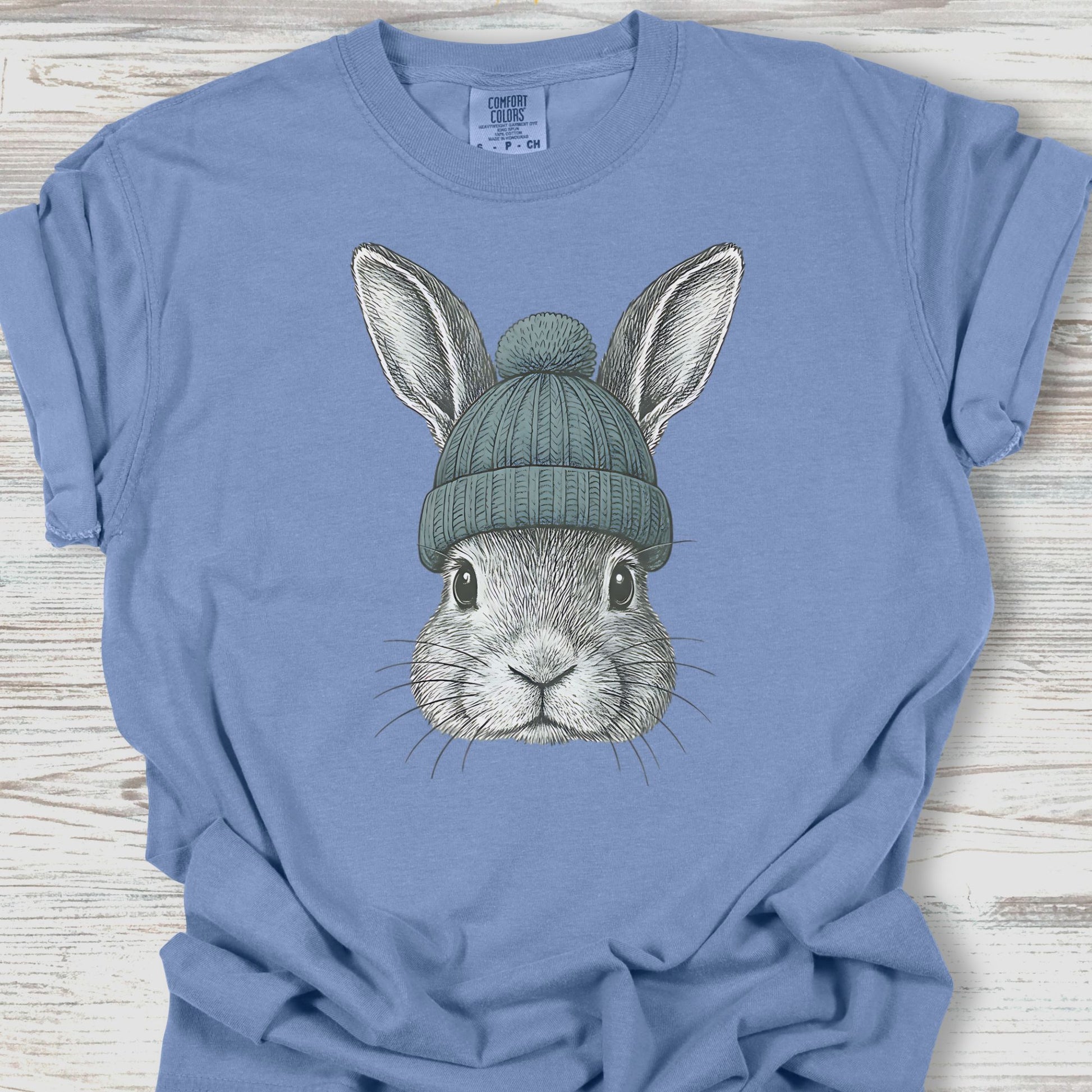Blue t-shirt with a graphic of a rabbit wearing a green beanie on a wooden surface