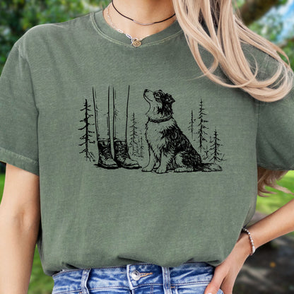 Person wearing a green t-shirt with a graphic of a dog, boots, and trees.