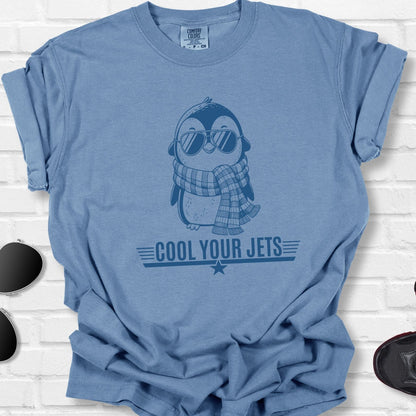 Blue t-shirt with penguin graphic and text 'Cool Your Jets' on a white brick background.