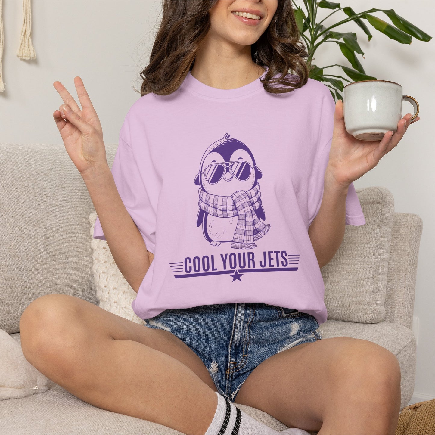 Person wearing a purple t-shirt with a penguin graphic and text, sitting on a couch holding a mug.
