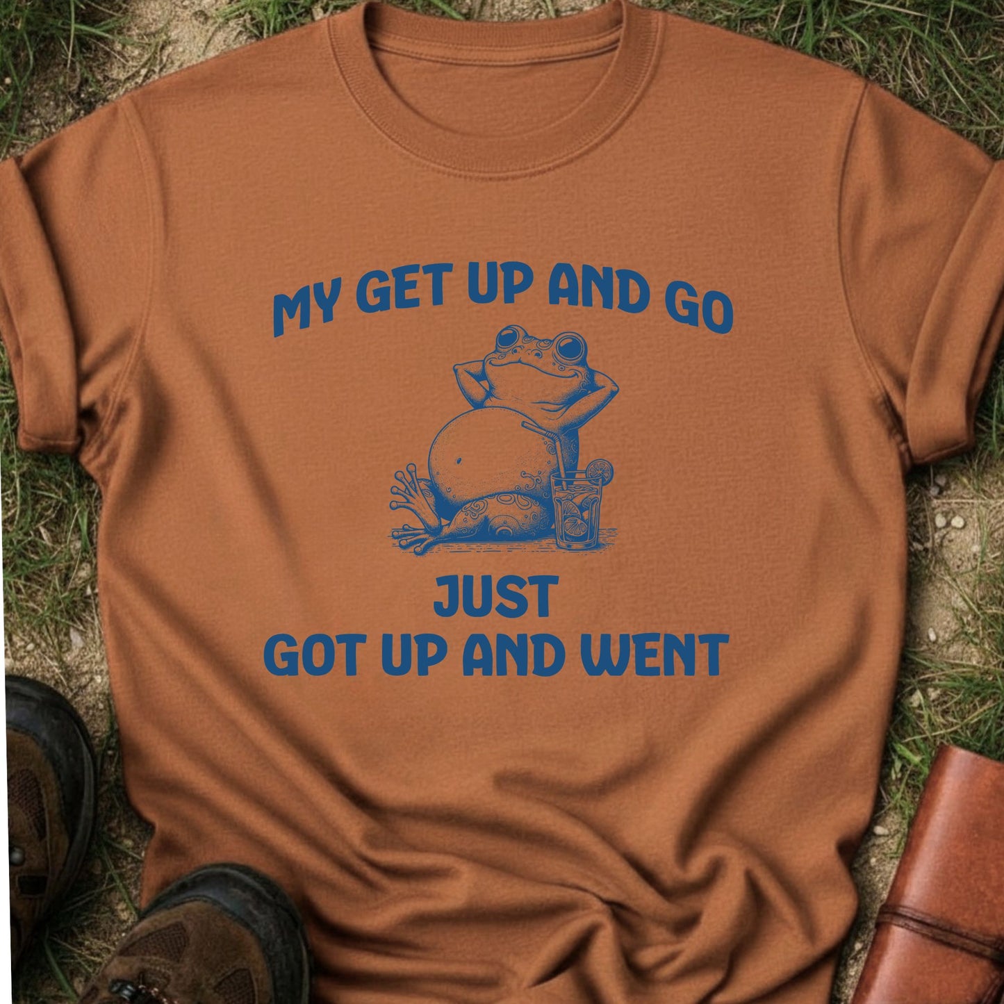 Brown t-shirt with a blue frog graphic and text on grass