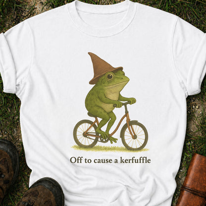 White t-shirt with a frog riding a bicycle graphic and text 'Off to cause a kerfuffle' on grass.