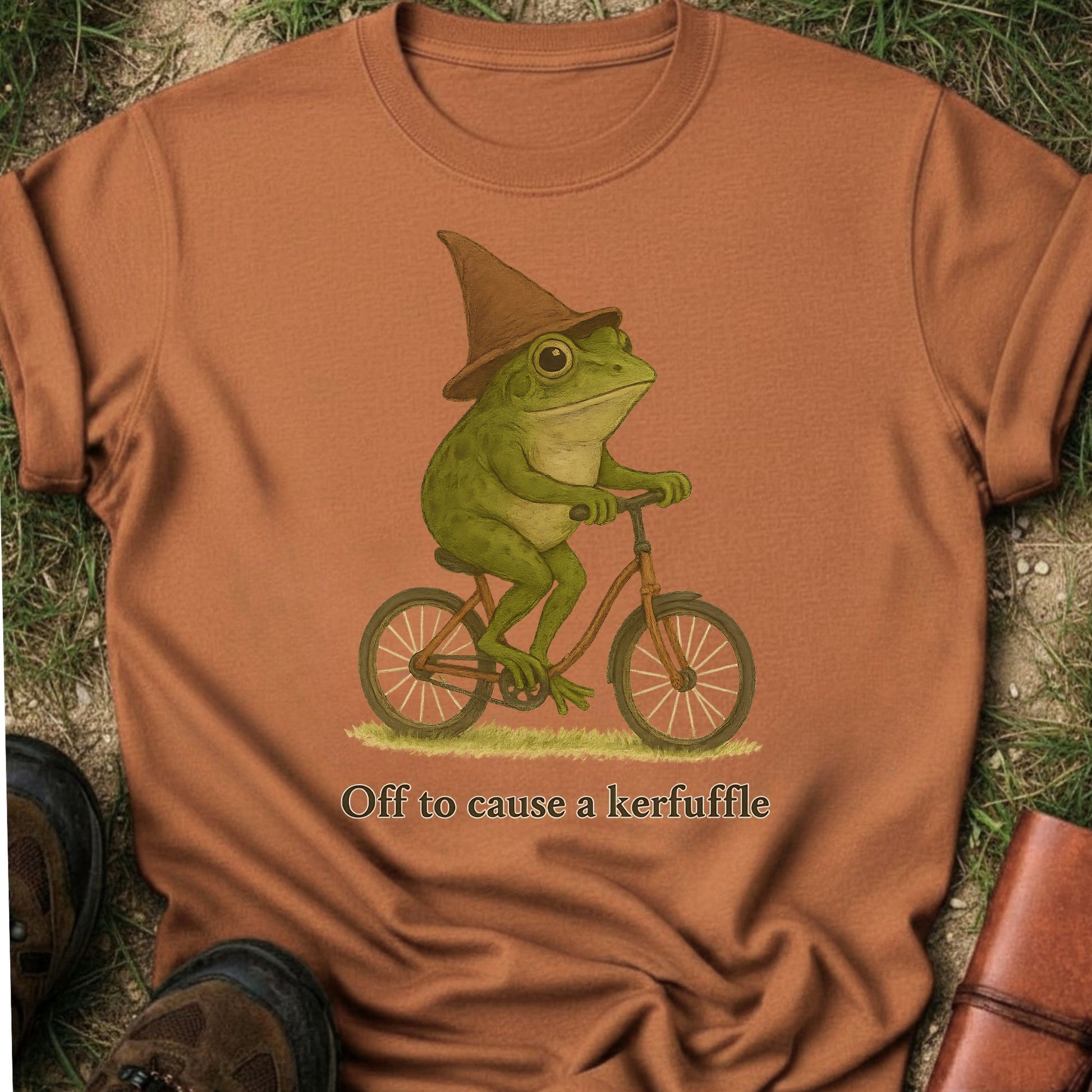 Orange t-shirt with a frog riding a bike graphic and text on grass.