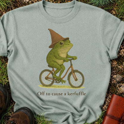 Light green t-shirt with a frog wearing a witch hat riding a bicycle graphic and text 'Off to cause a kerfuffle'.