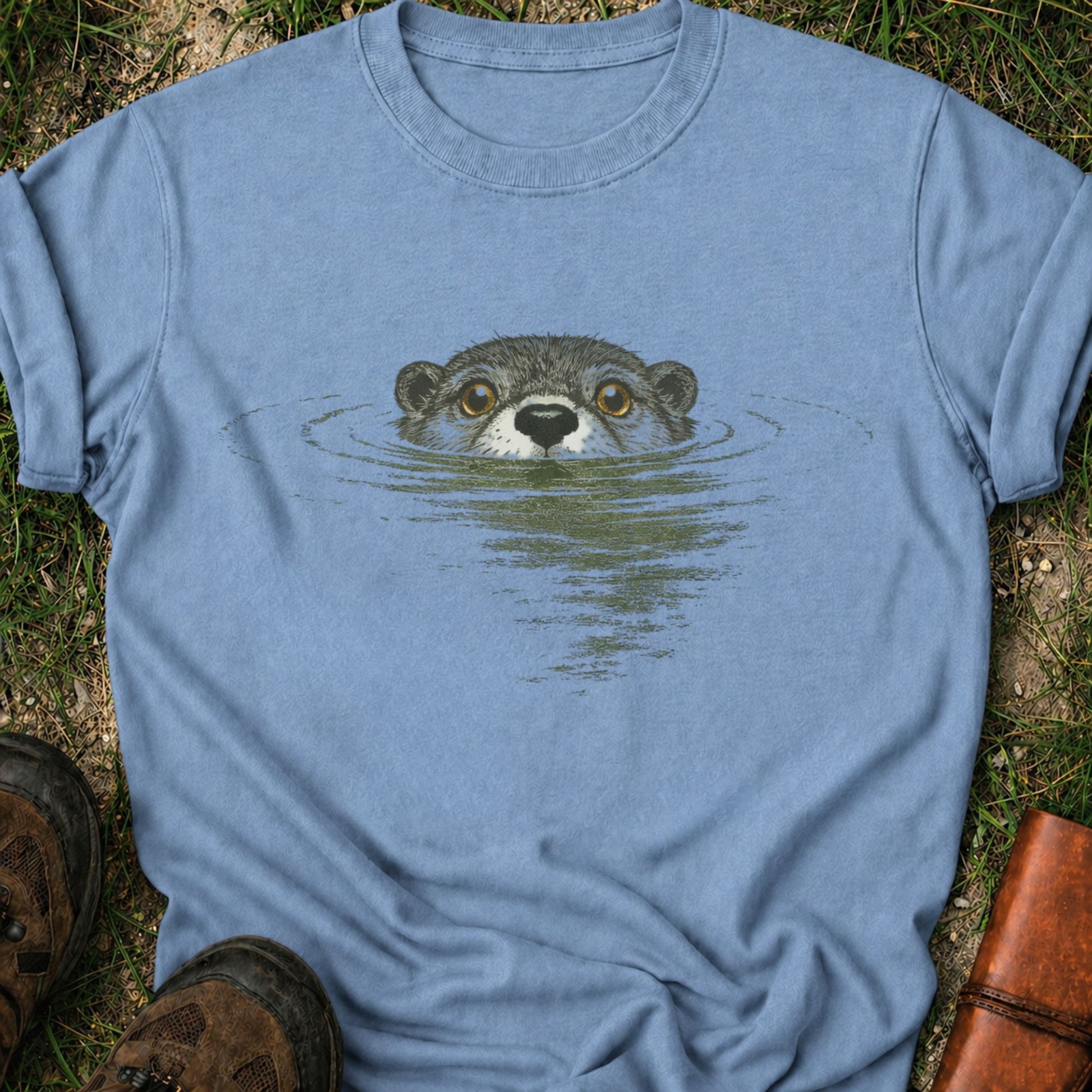 Blue T-shirt with swimming otter design on lyimg on a grassy surface