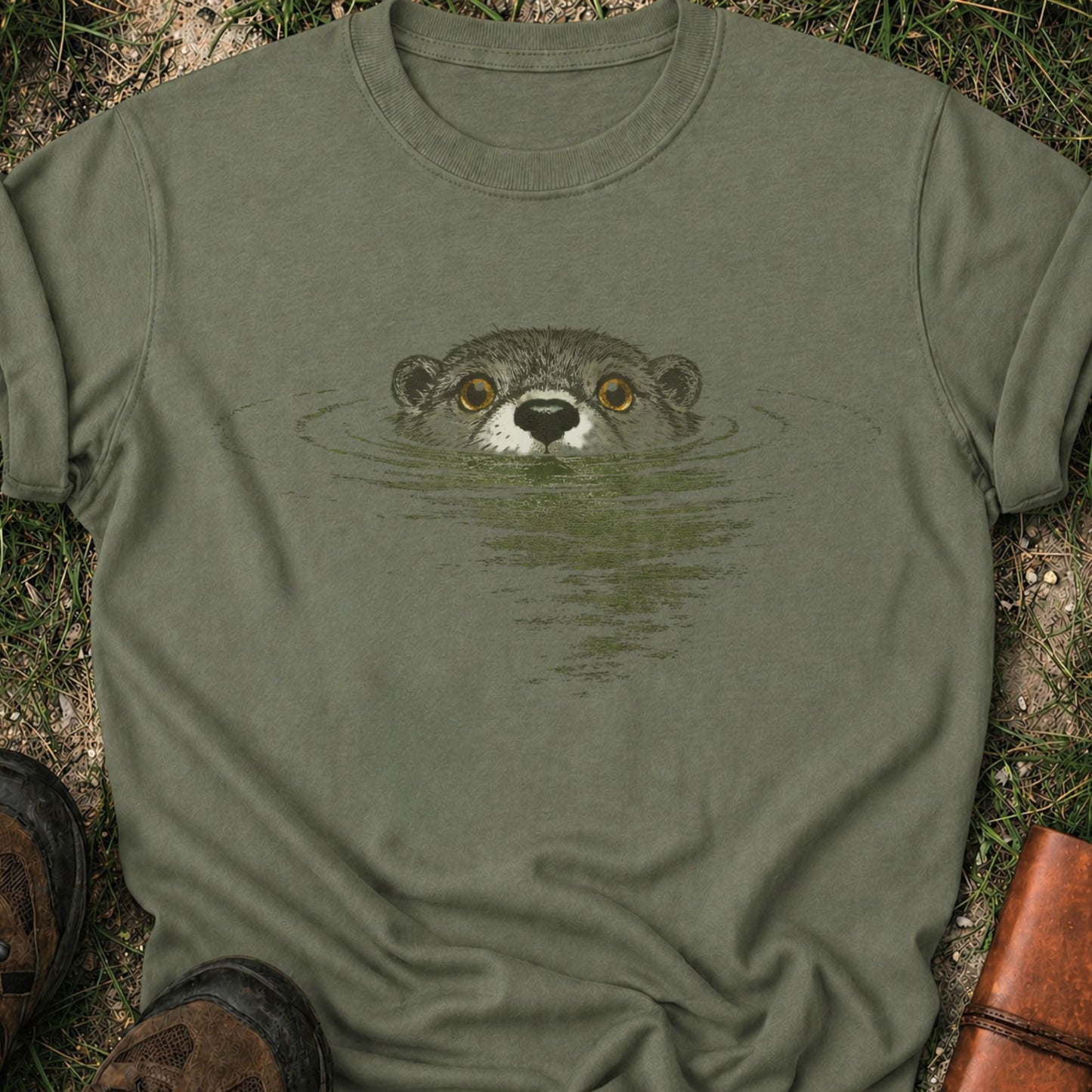 Darker green T-shirt with swimming otter design on lyimg on a grassy surface