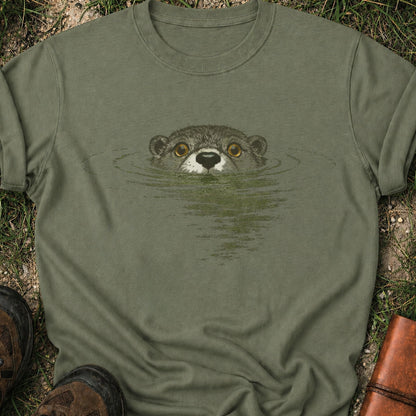Darker green T-shirt with swimming otter design on lyimg on a grassy surface