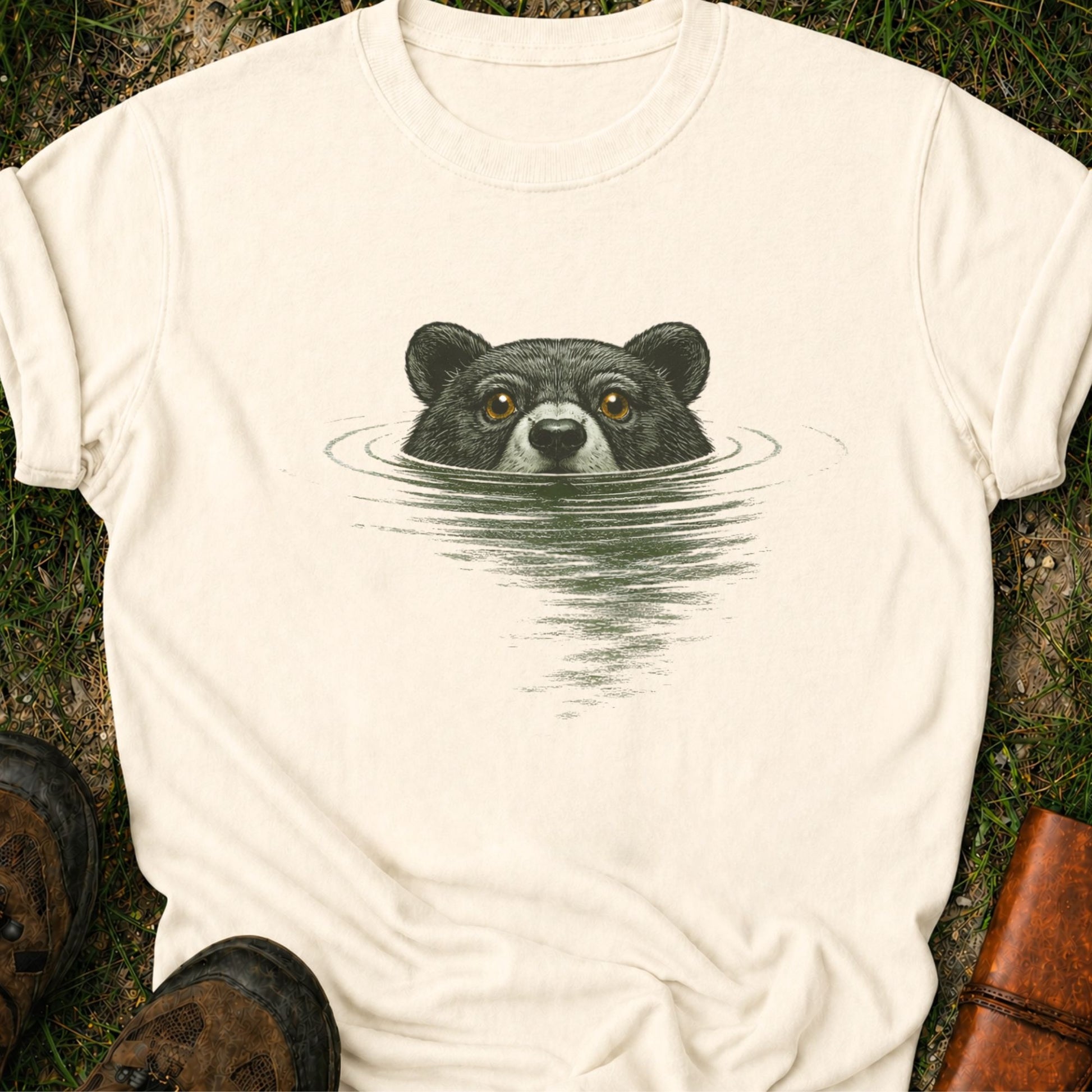 Ivory t-shirt with a bear swimming graphic lying on a grassy surface