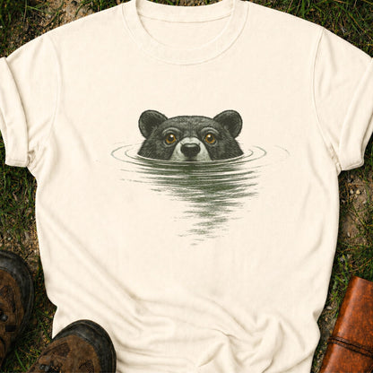 Ivory t-shirt with a bear swimming graphic lying on a grassy surface