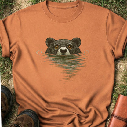 Orange T-shirt with a swimming bear  graphic lying on a grassy surface
