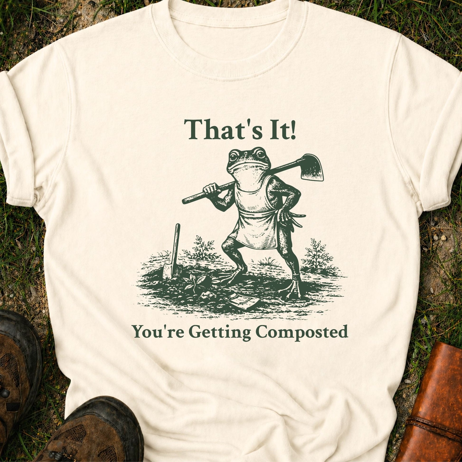 Ivory Tshirt lying on a grassy surface.  Graphic is a frog with a hand on his hip holding a hoe with the tagline "That's It!, You're Getting Composted.