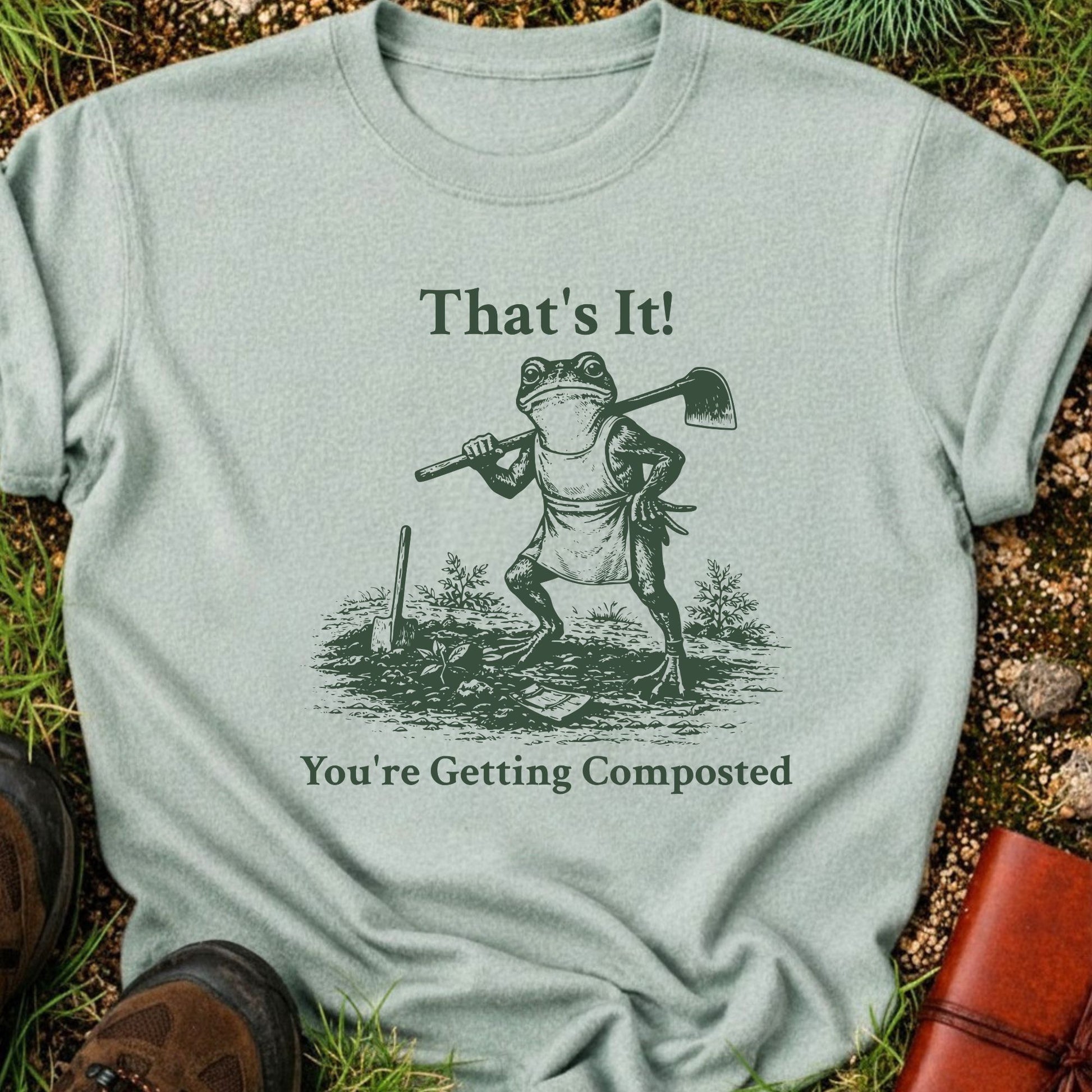 Green Tshirt lying on a grassy surface.  Graphic is a frog with a hand on his hip holding a hoe with the tagline "That's It!, You're Getting Composted.