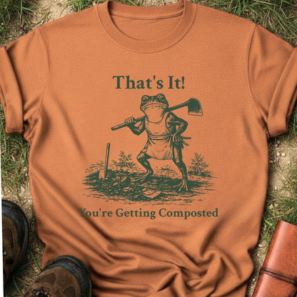 Orange Tshirt lying on a grassy surface.  Graphic is a frog with a hand on his hip holding a hoe with the tagline "That's It!, You're Getting Composted.