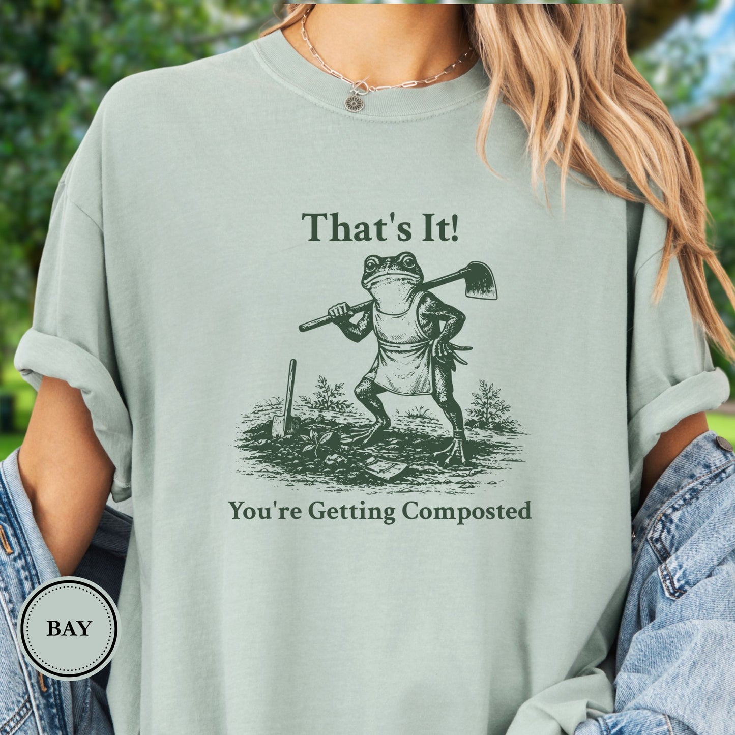 Model wearing a green T-shirt.  Graphic is a frog with a hand on his hip holding a hoe with the tagline "That's It!, You're Getting Composted.