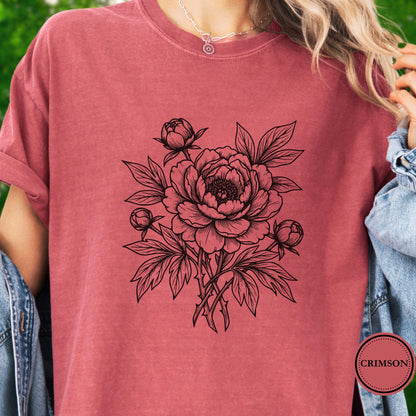 Model wears a dark pink Tshirt. The black graphic on the shirt is a  botanical line art design featuring a detailed peony-style flower with leaves and buds. 