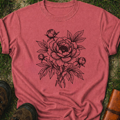 Dark Pink Tshirt lying on a grassy surface. The black graphic on the shirt is an  botanical line art design featuring a detailed peony-style flower with leaves and buds.