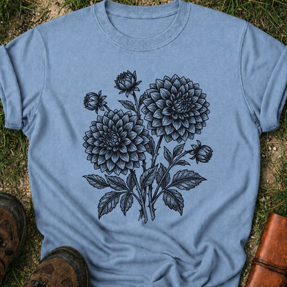 Blue T-Shirt laying on a grassy surface.  The graphic features a minimal black botanical line art design featuring dahlias with leafy stems and delicate floral details.