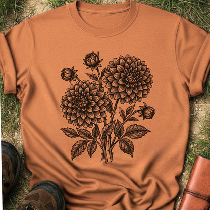 Orange T-Shirt laying on a grassy surface.  The graphic features a minimal black botanical line art design featuring dahlias with leafy stems and delicate floral details.