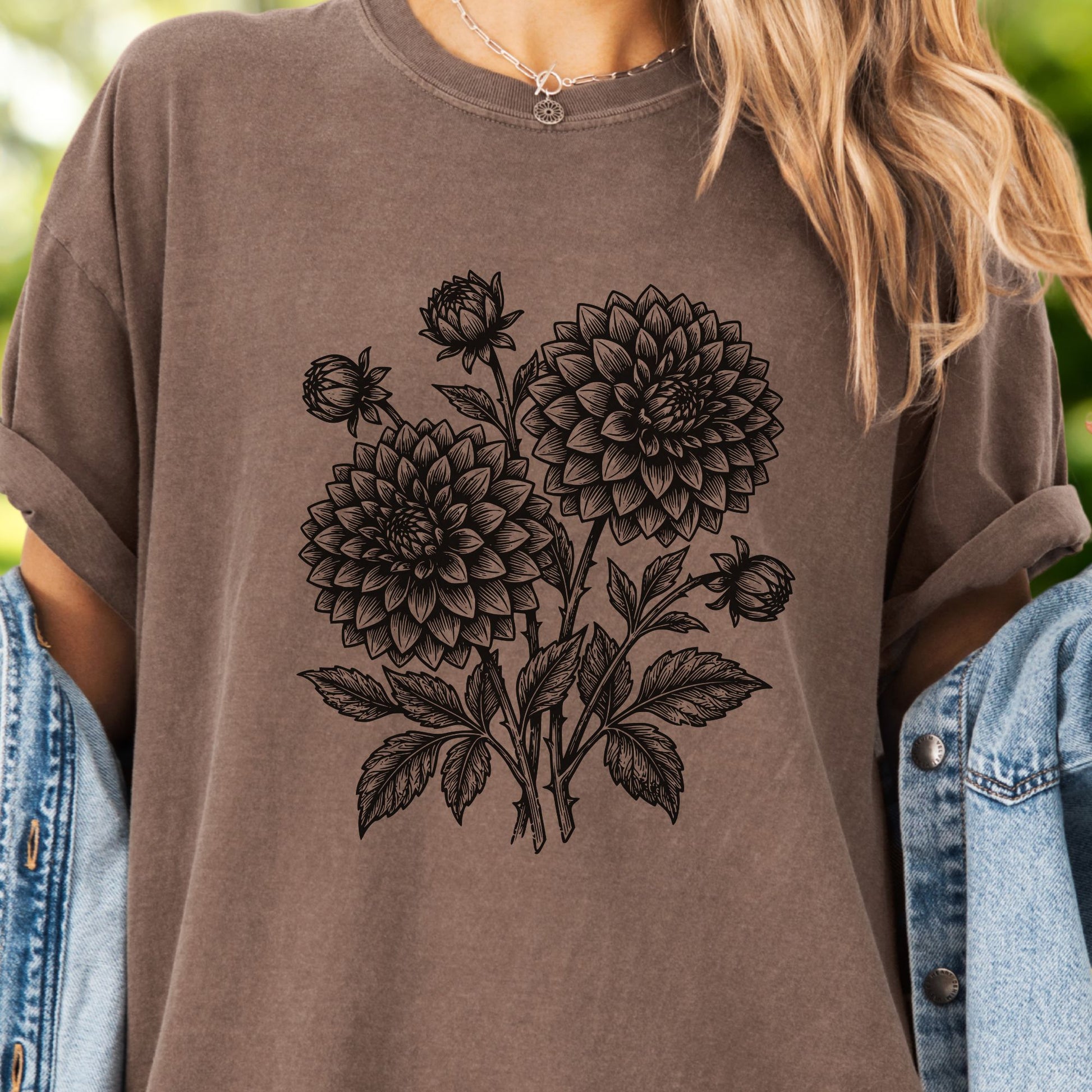 Model wears a brown T-Shirt -  the graphic features a minimal black botanical line art design featuring dahlias with leafy stems and delicate floral details.