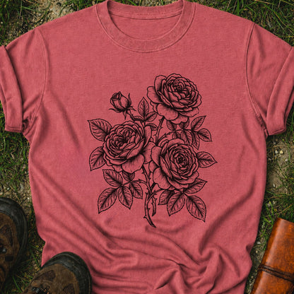 Dark Pink Tshirt lying on a grassy surface.  Graphic shows minimal black botanical line art design featuring elegant roses with leafy stems