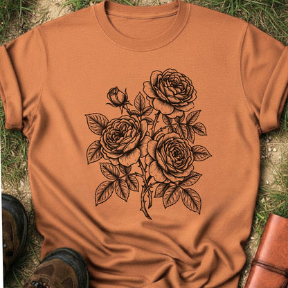 Ornge Tshirt lying on a grassy surface.  Graphic shows minimal black botanical line art design featuring elegant roses with leafy stems