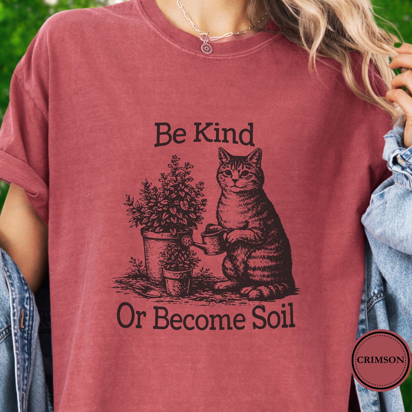 Model wears a dark pink t-shirt, the graphic is a Funny vintage-style gardening cat design featuring a cat watering plants with the phrase “Be Kind Or Become Soil.”