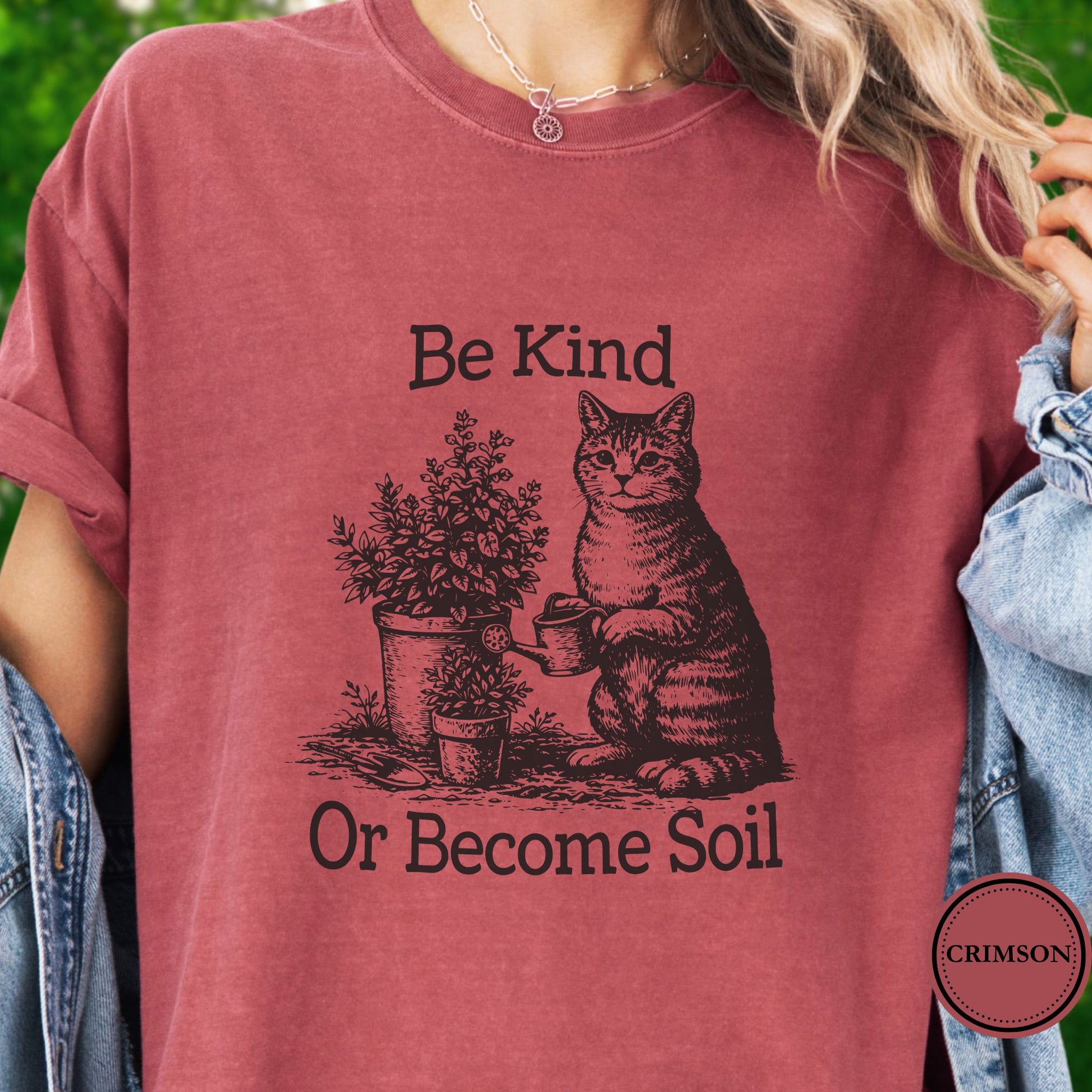 Model wears a dark pink t-shirt, the graphic is a Funny vintage-style gardening cat design featuring a cat watering plants with the phrase “Be Kind Or Become Soil.”