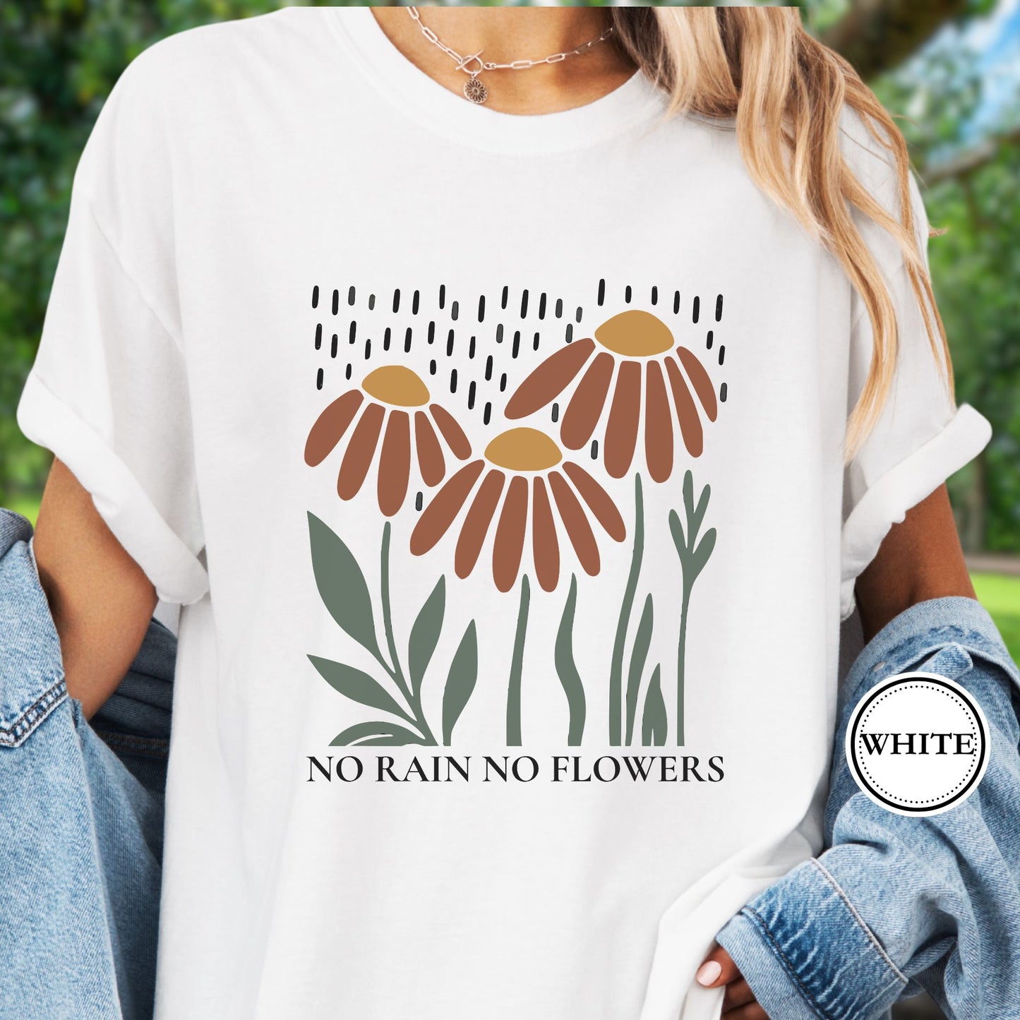 Model wears a white T-shirt featuring earthy red and gold blooms with muted green stems with text reading No Rain, No Flowers. 