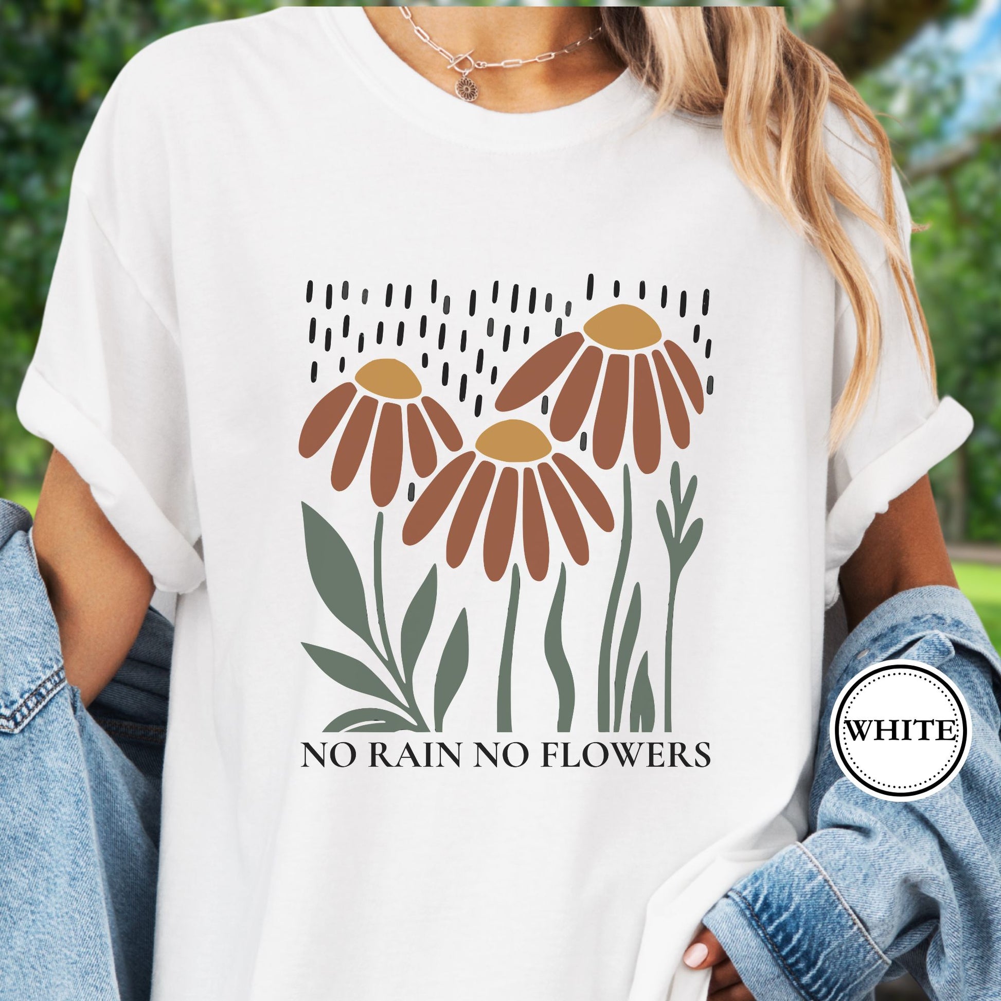Model wears a white T-shirt featuring earthy red and gold blooms with muted green stems with text reading No Rain, No Flowers. 